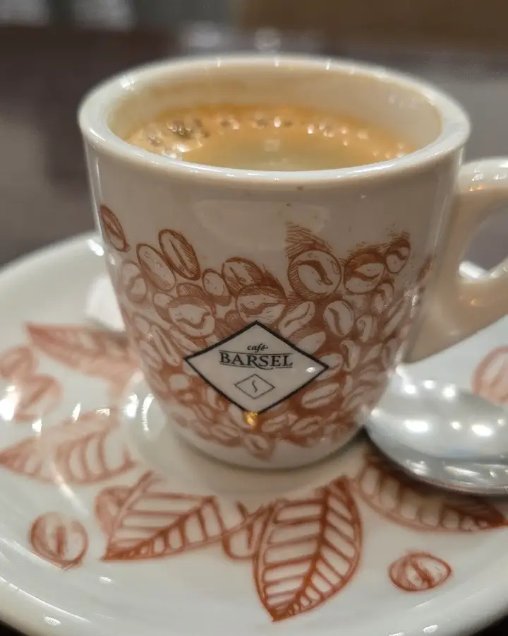Un café solo en la taza de la casa, con el plato estampado de hojas y granos de café