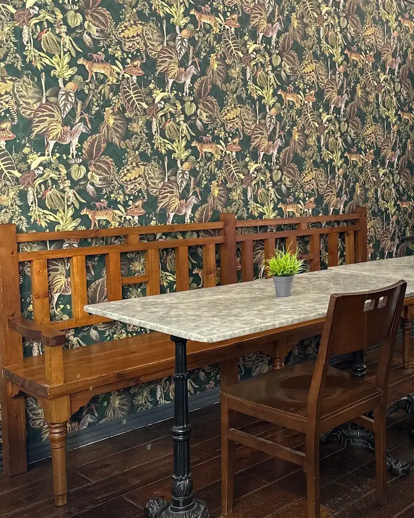 La pared de papel pintado de selva de Conrin Coffee, con el banco de madera tallada y una mesa de mármol
