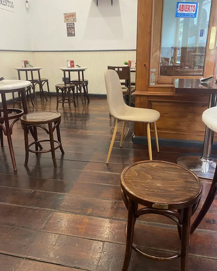 Un taburete de madera curvada sobre el suelo de tablas oscuras, junto a la puerta con el cartel de abierto